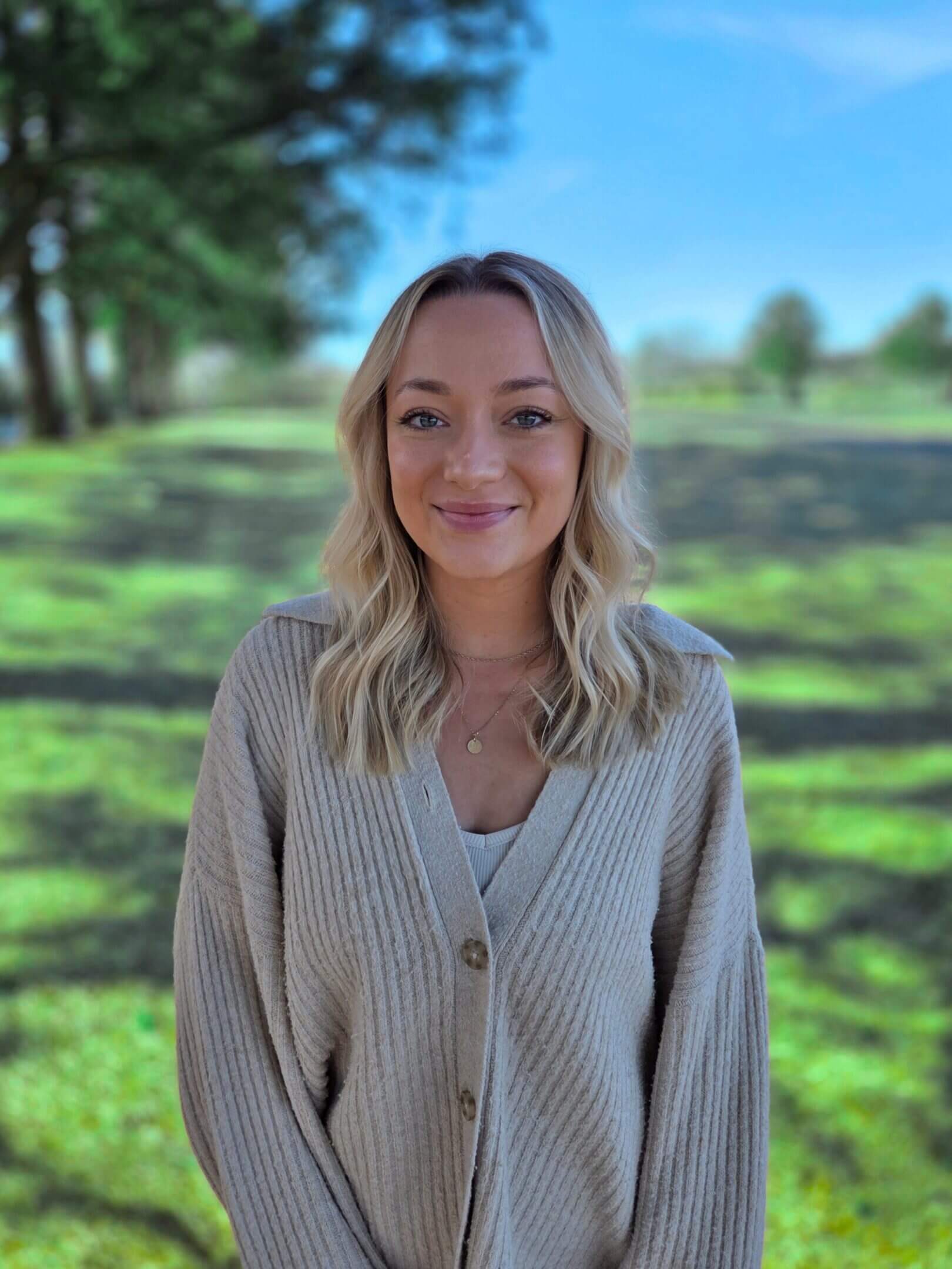 Smiling woman standing in sunny park.